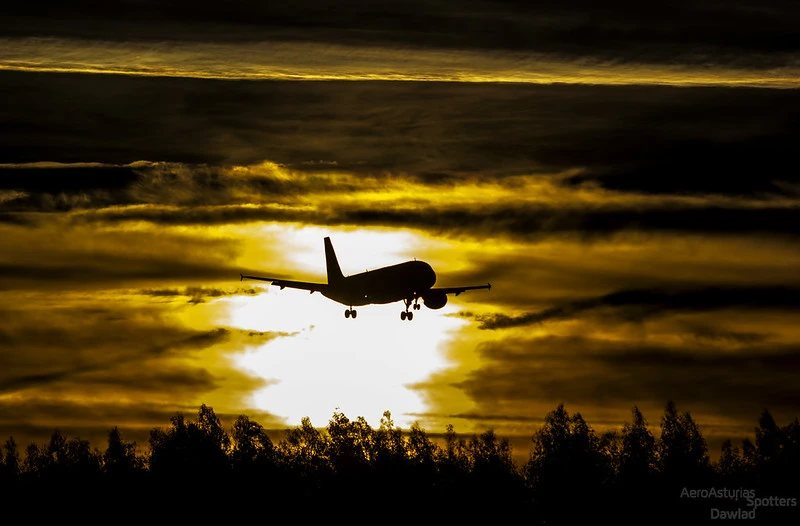 Silueta de un Airbus A320 de Vueling con el tren desplegado al amanecer sobre el Aeropuerto de Asturias